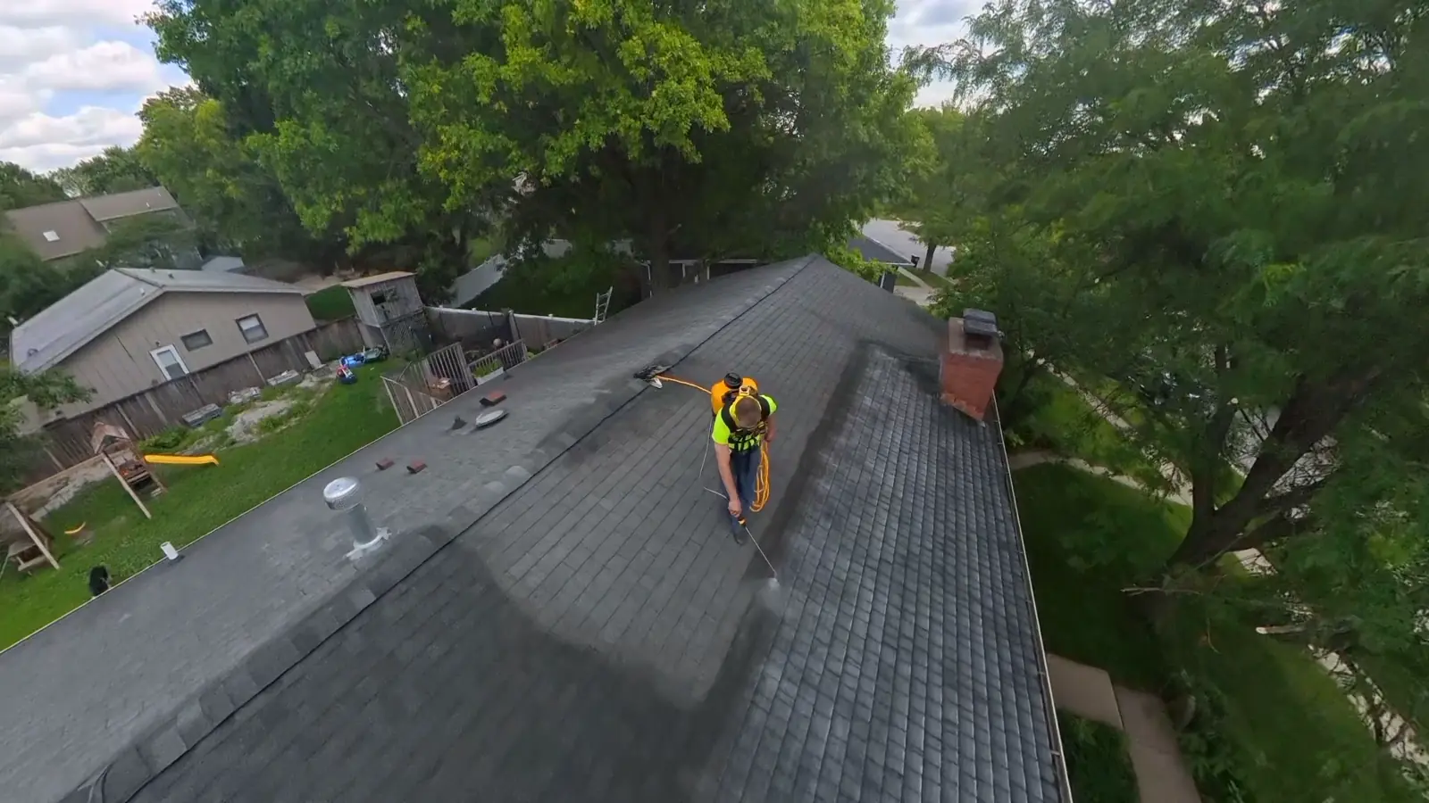Aerial view of an asphalt roof mid-application, treated area visibly darker