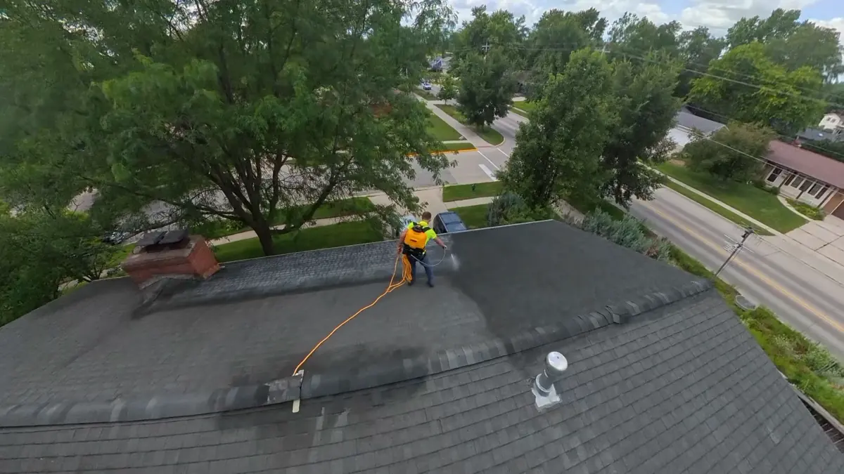 Top-down aerial of applicator spraying an asphalt roof