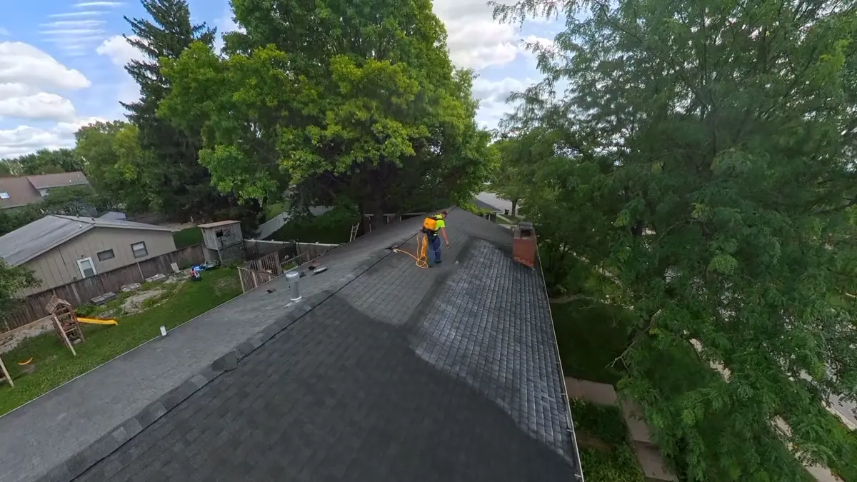 Applicator working across a shingle roof with spray equipment