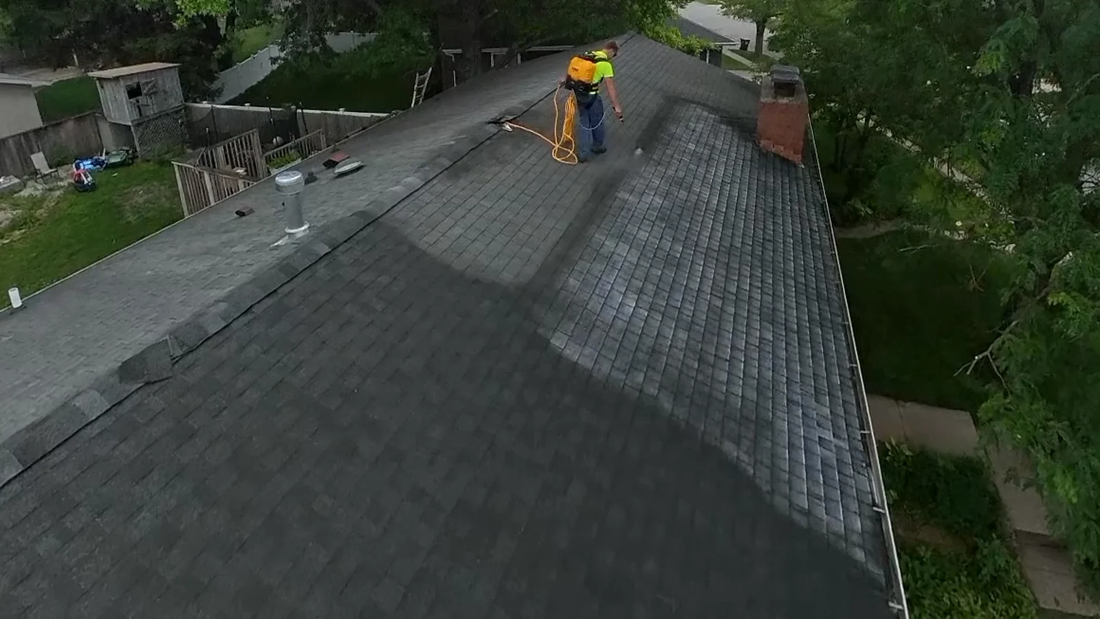Aerial view of an applicator on the ridge where the treated dark half of the roof meets the untreated pale half