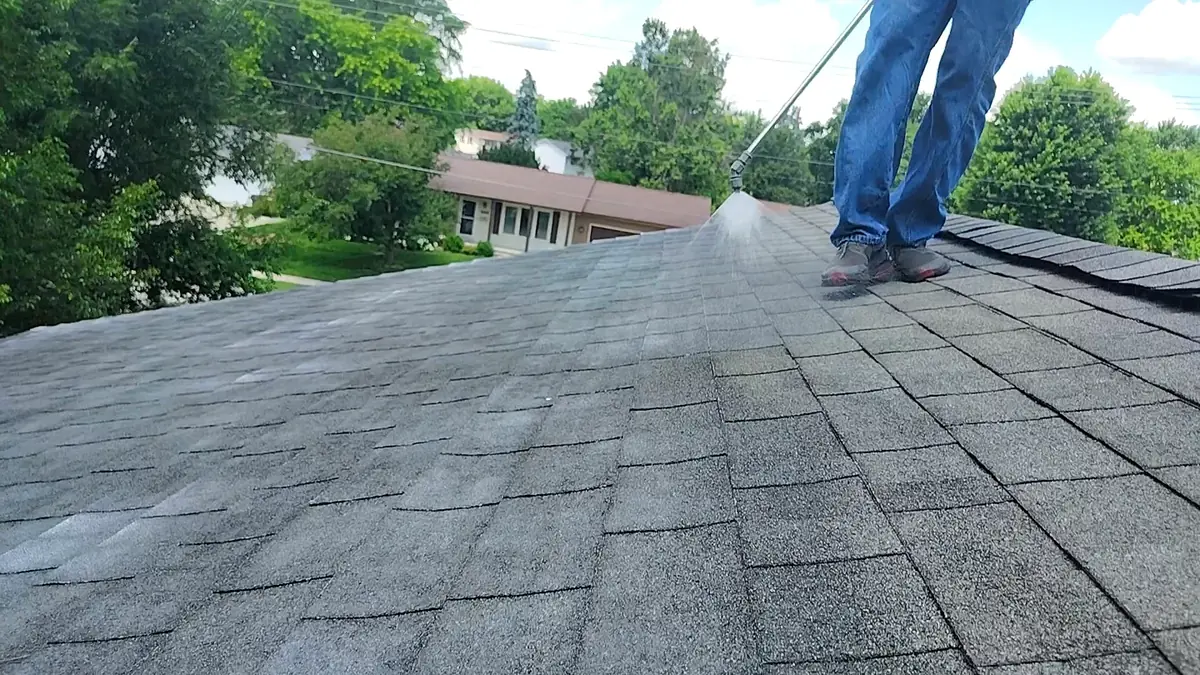 Applicator spraying soy-based treatment along the ridge of a shingle roof in full sun